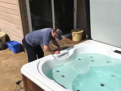 Worker leaning over an old hot tub on a wooden deck, getting it ready to be removed